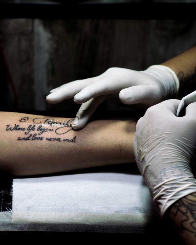 Gloved hands wiping a fresh script tattoo on a forearm